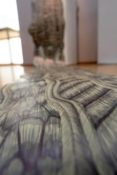 Le chemin dessiné vu au ras du sol, fuyant vers la lumière de la salle.