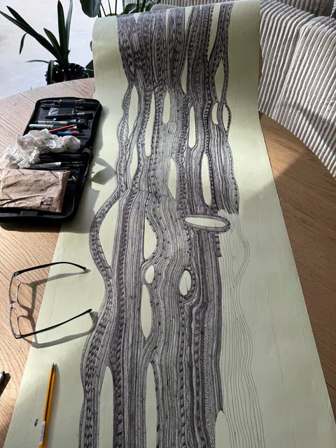 La bande de papier en cours de dessin sur une table, à côté des stylos et des lunettes.