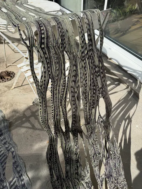 Bandes de papier dessinées et découpées, dont les ombres se projettent sur la terrasse.
