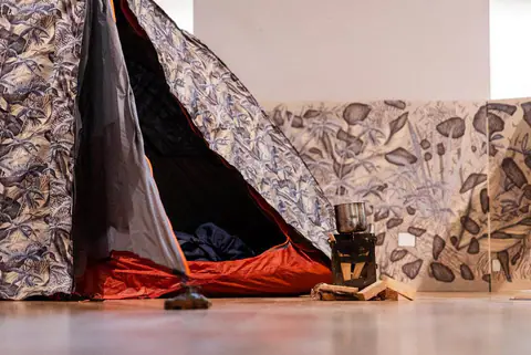 Entrée de la tente ouverte, sac de couchage rouge à l'intérieur, panneau dessiné au sol.